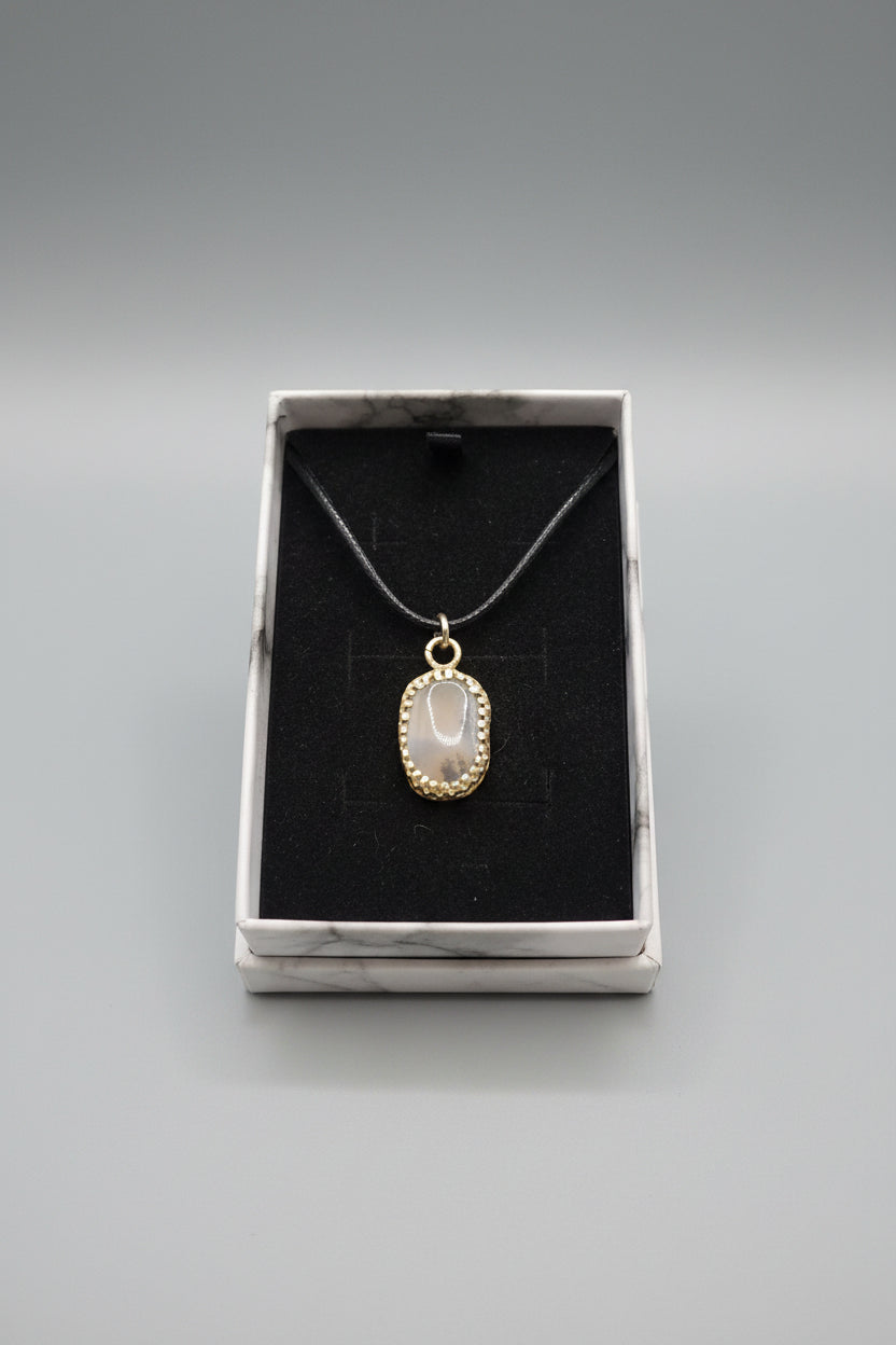 A silver-toned oval pendant necklace with a pale gray stone, displayed inside an open white gift box with a black velvet insert.