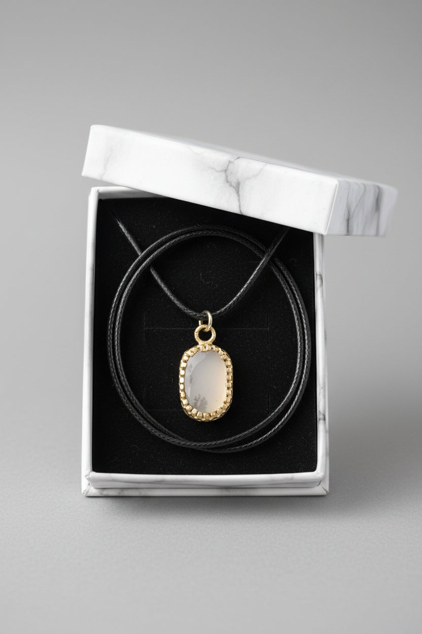 A silver-toned oval pendant necklace with a pale translucent stone, displayed inside an open white gift box with a black velvet insert.