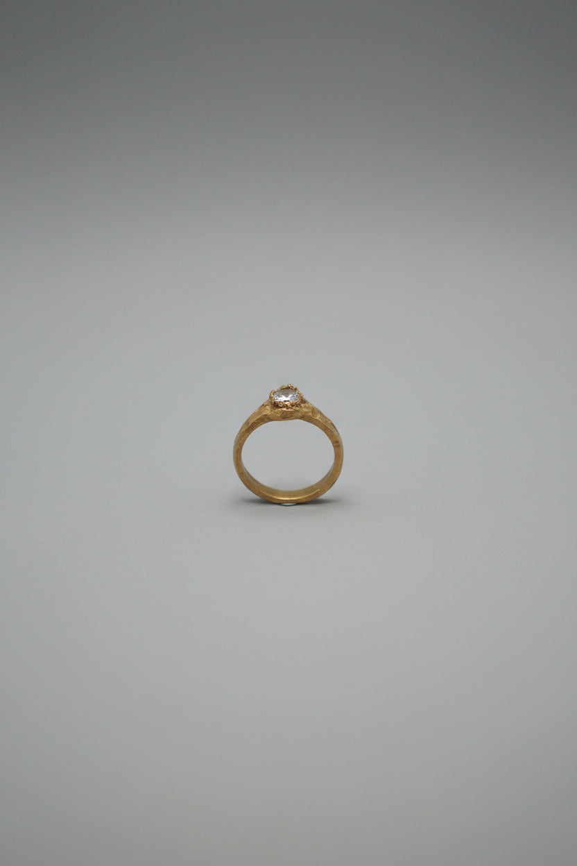 A gold ring with a clear round gemstone displayed on a wooden jewelry organizer with dark blue felt compartments.