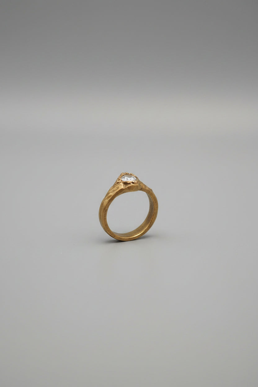 A gold ring with a clear round gemstone displayed on a black stand inside a wooden 9-compartment jewelry organizer.