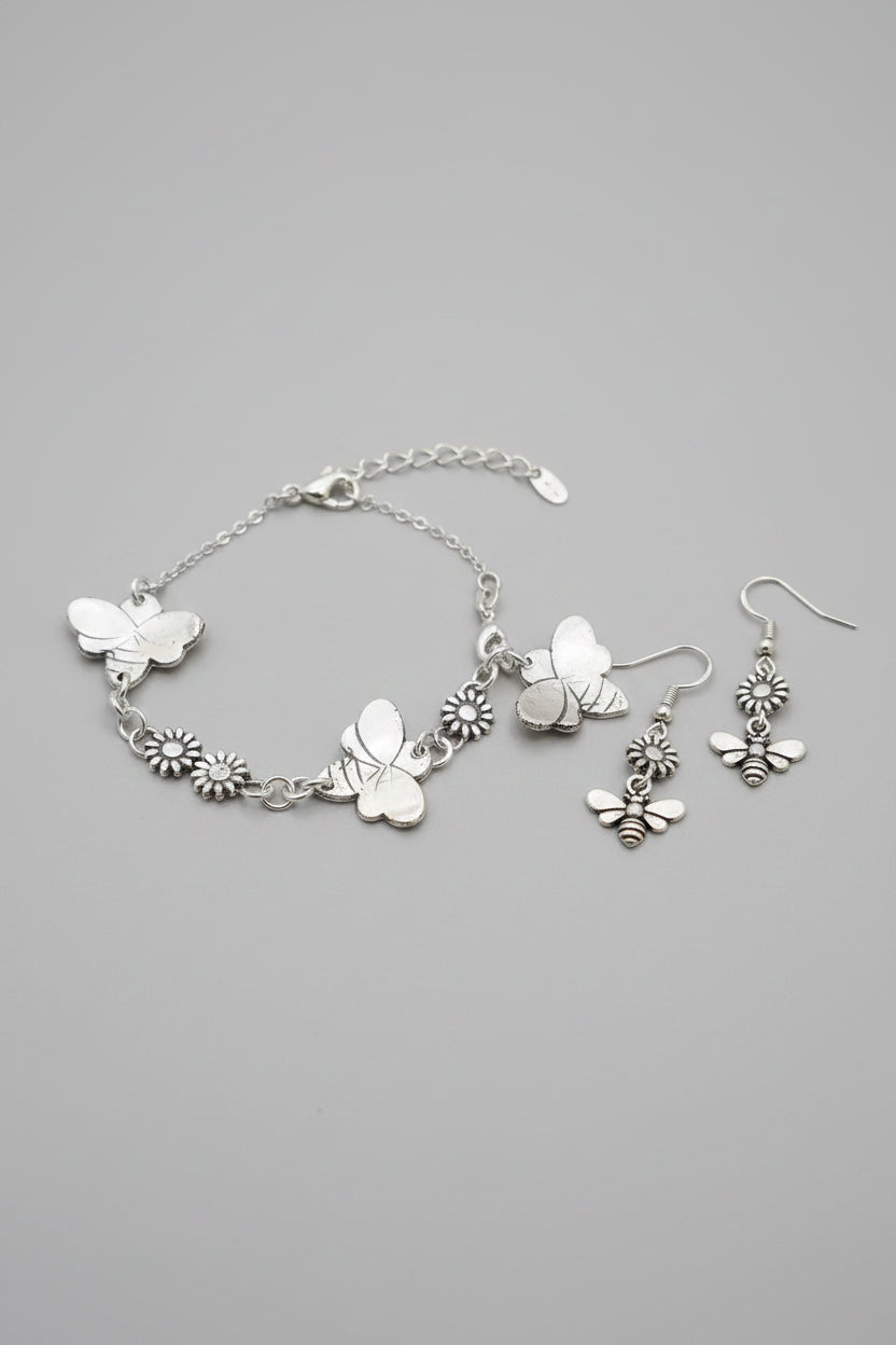 A silver charm bracelet featuring butterfly and daisy charms, displayed on a textured gray fabric surface.
