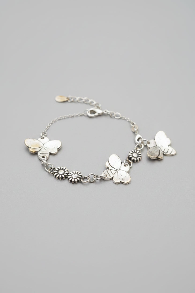 A silver chain bracelet with butterfly and flower charms, displayed on a textured gray fabric surface.