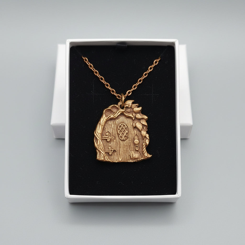 A copper -toned fantasy door pendant necklace displayed inside an open jewelry box with a black insert, set on a gray textured surface with jewelry trays in the background.