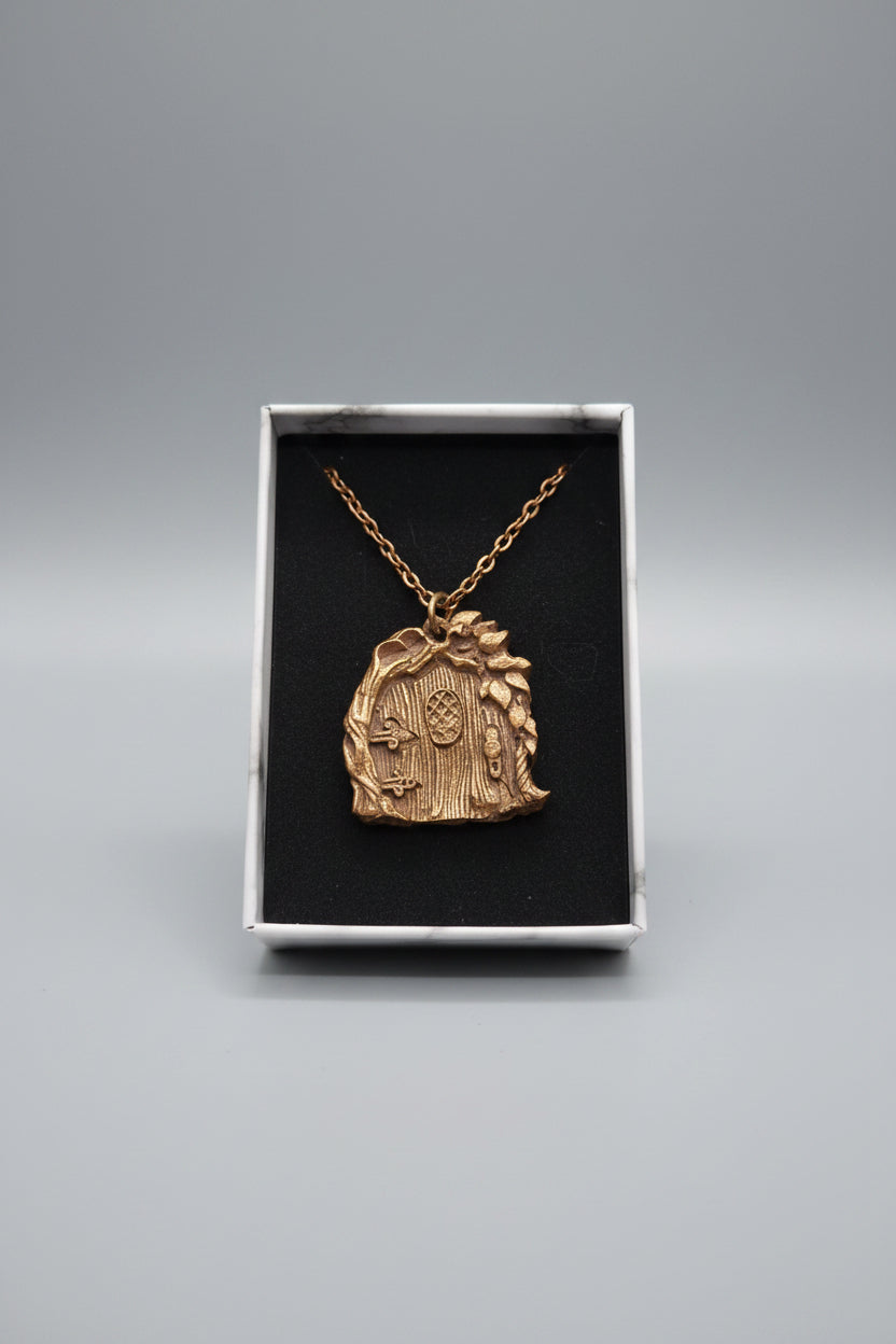 A copper-toned fantasy door pendant necklace displayed inside an open jewelry box with a black insert, set on a textured gray surface with a wooden display tray in the background.