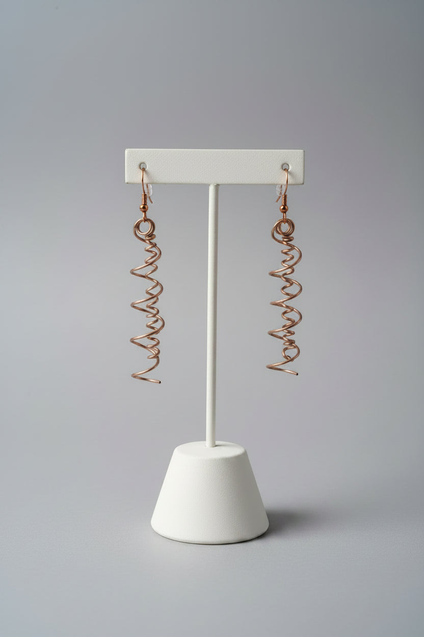 A pair of handmade copper wire dangle earrings with a coiled spring design, displayed on a textured gray fabric background.