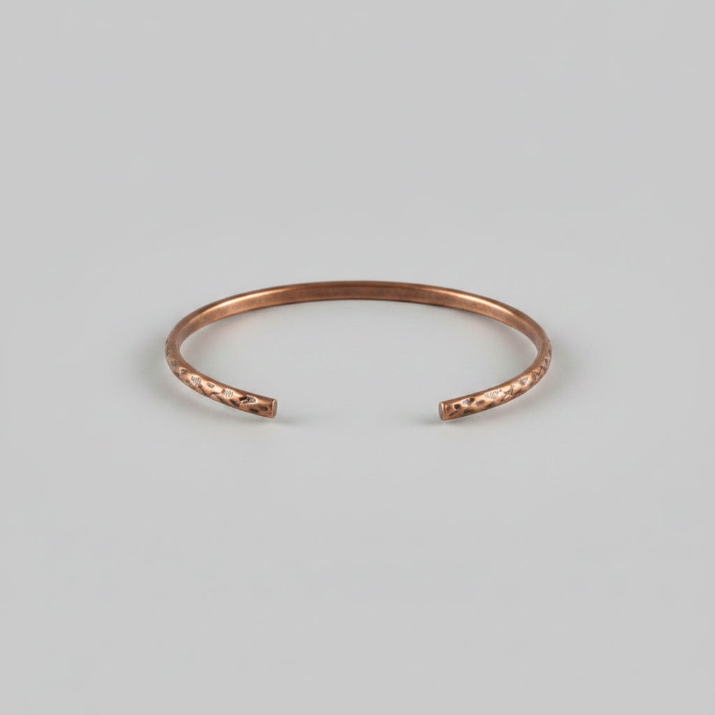 A hammered copper-toned metal cuff bracelet resting on a textured gray fabric surface.