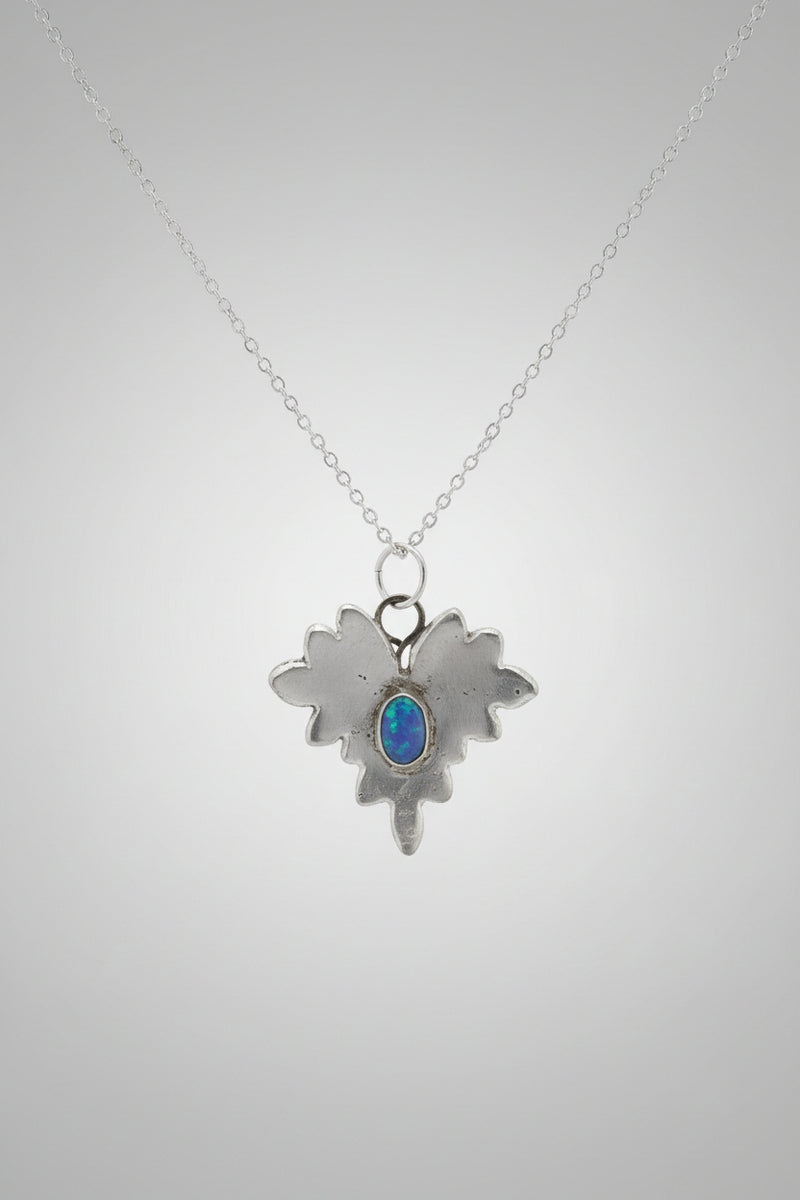 A silver-toned pendant necklace with a textured, leaf-like or flame-like silhouette and a small oval blue stone in the center, displayed on a burlap-covered jewelry bust.