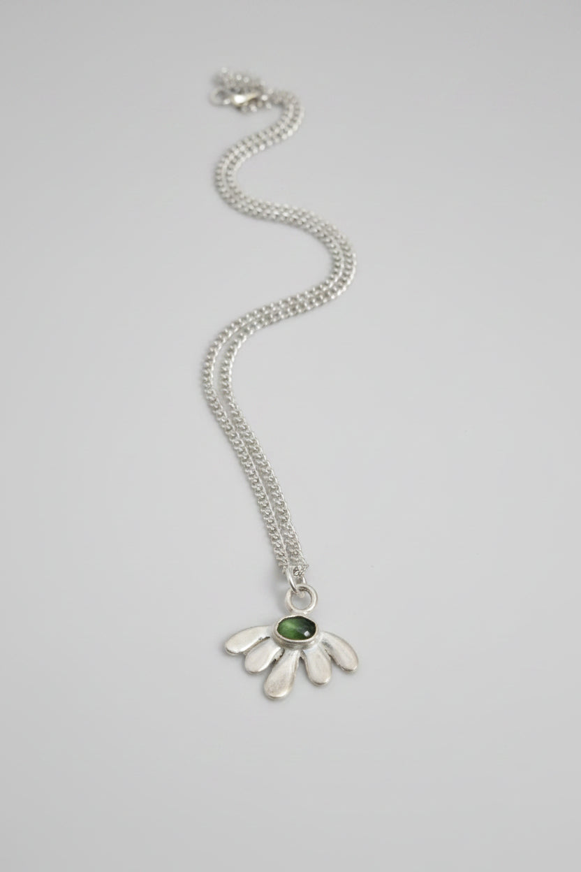 A sterling silver daisy pendant necklace with a green gemstone center, displayed on a textured dark brown surface.