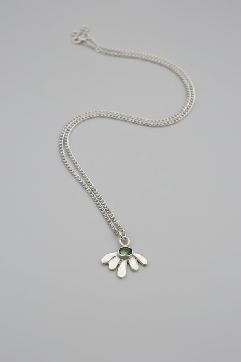 A sterling silver hamsa hand pendant necklace with a small green gemstone in the center, resting on a textured dark brown surface.