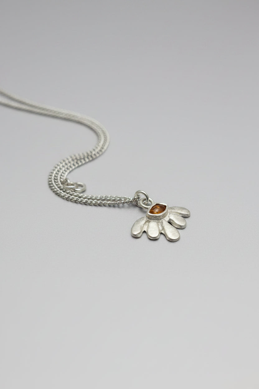 A sterling silver daisy pendant necklace with a small amber gemstone in the center, resting on a textured dark brown leather surface.