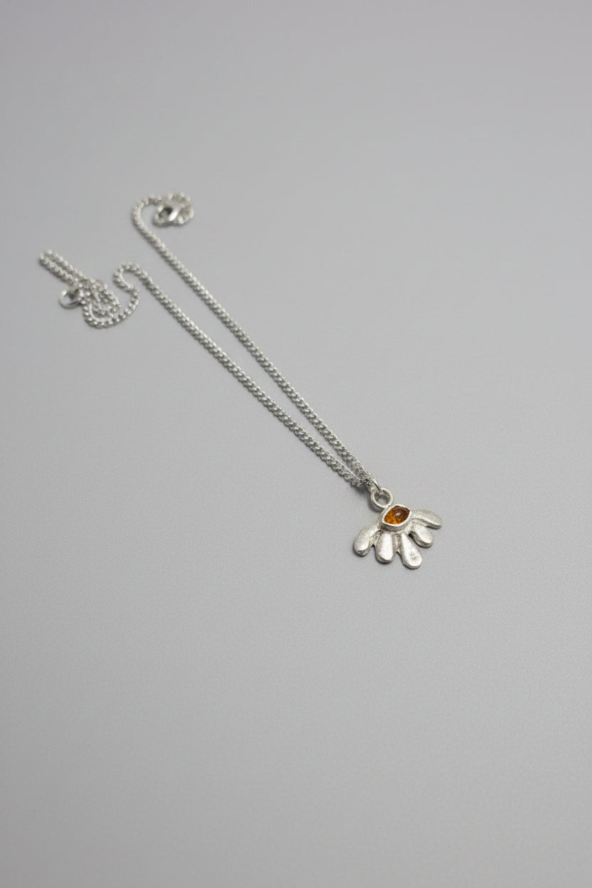 A sterling silver pendant necklace featuring a stylized flower with a small orange gemstone in the center, resting on a textured dark brown leather surface.