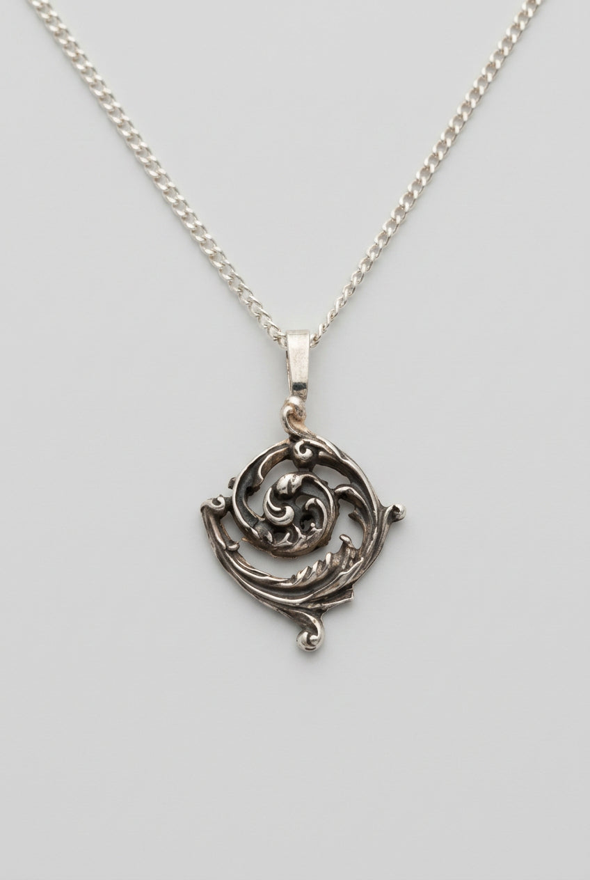 A close-up of a silver-toned filigree pendant necklace resting on a person's skin.