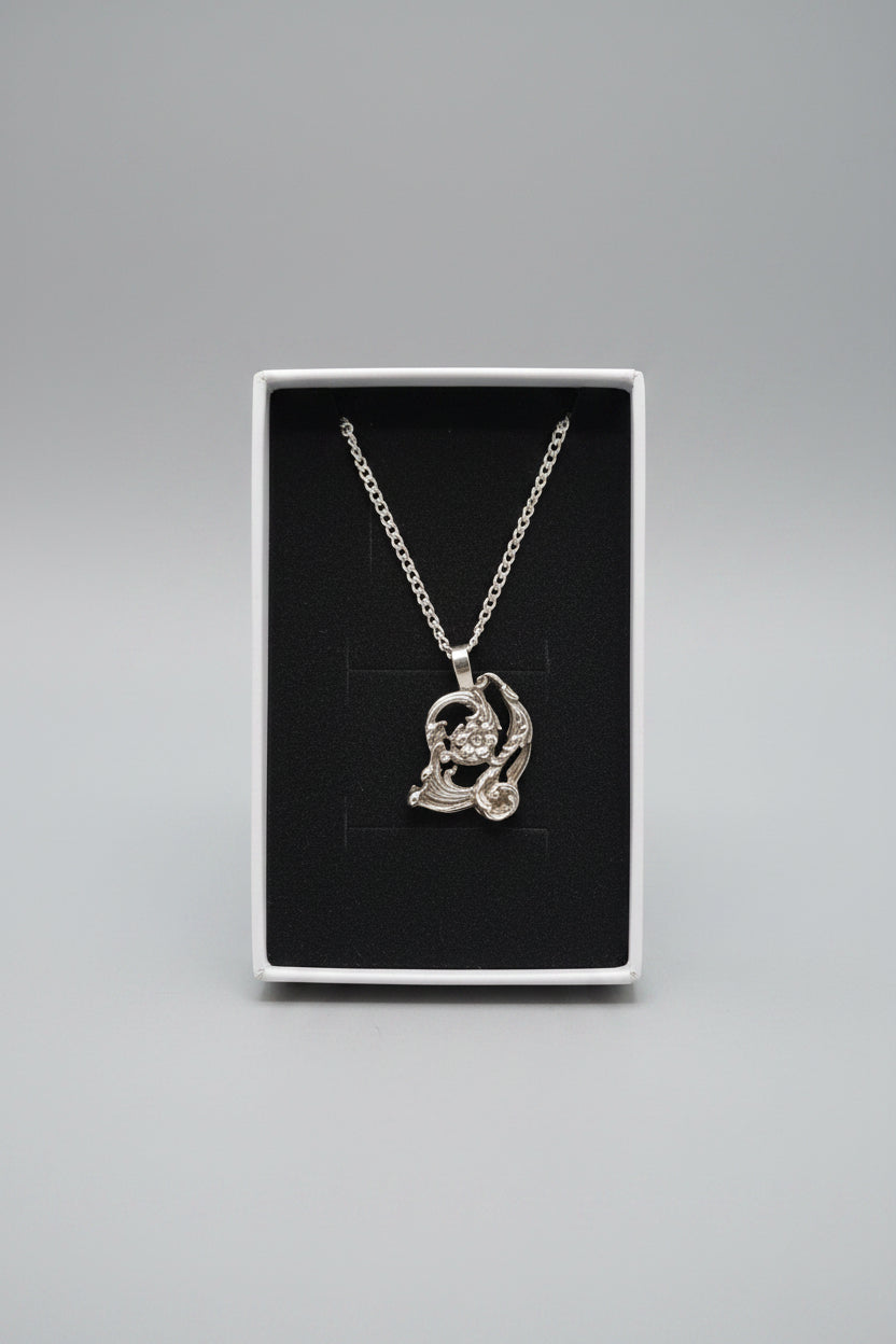 A silver-toned pendant necklace displayed inside an open white jewelry box with a black insert. The pendant appears to feature a crescent moon and star design with small clear stones.