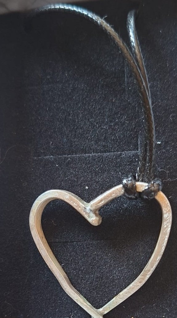 A silver heart-shaped fork prong pendant necklace with a black cord, displayed on a black textured background.