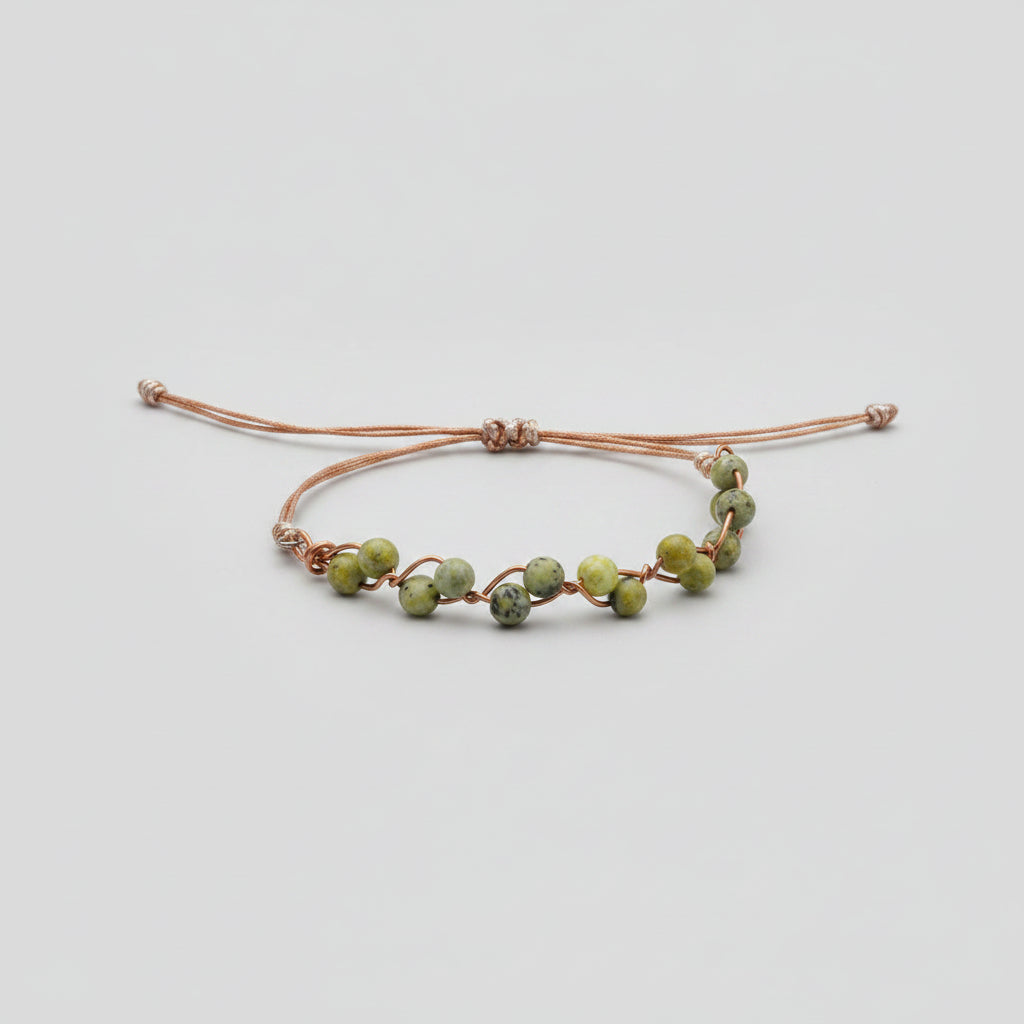 A copper wire bracelet with small green and yellow marbled beads, resting on a textured gray fabric surface.