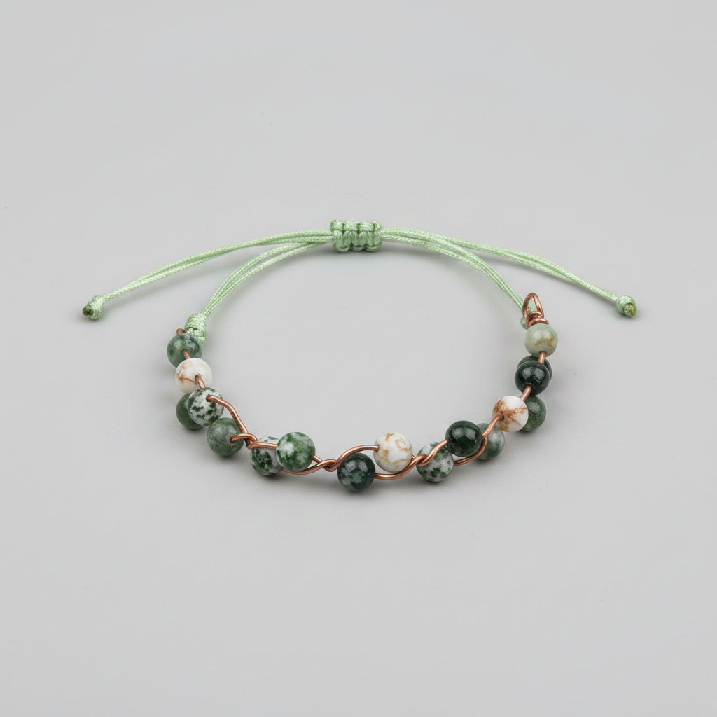A handmade beaded bracelet with green and white marbled beads connected by copper wire, resting on a gray textured fabric surface.