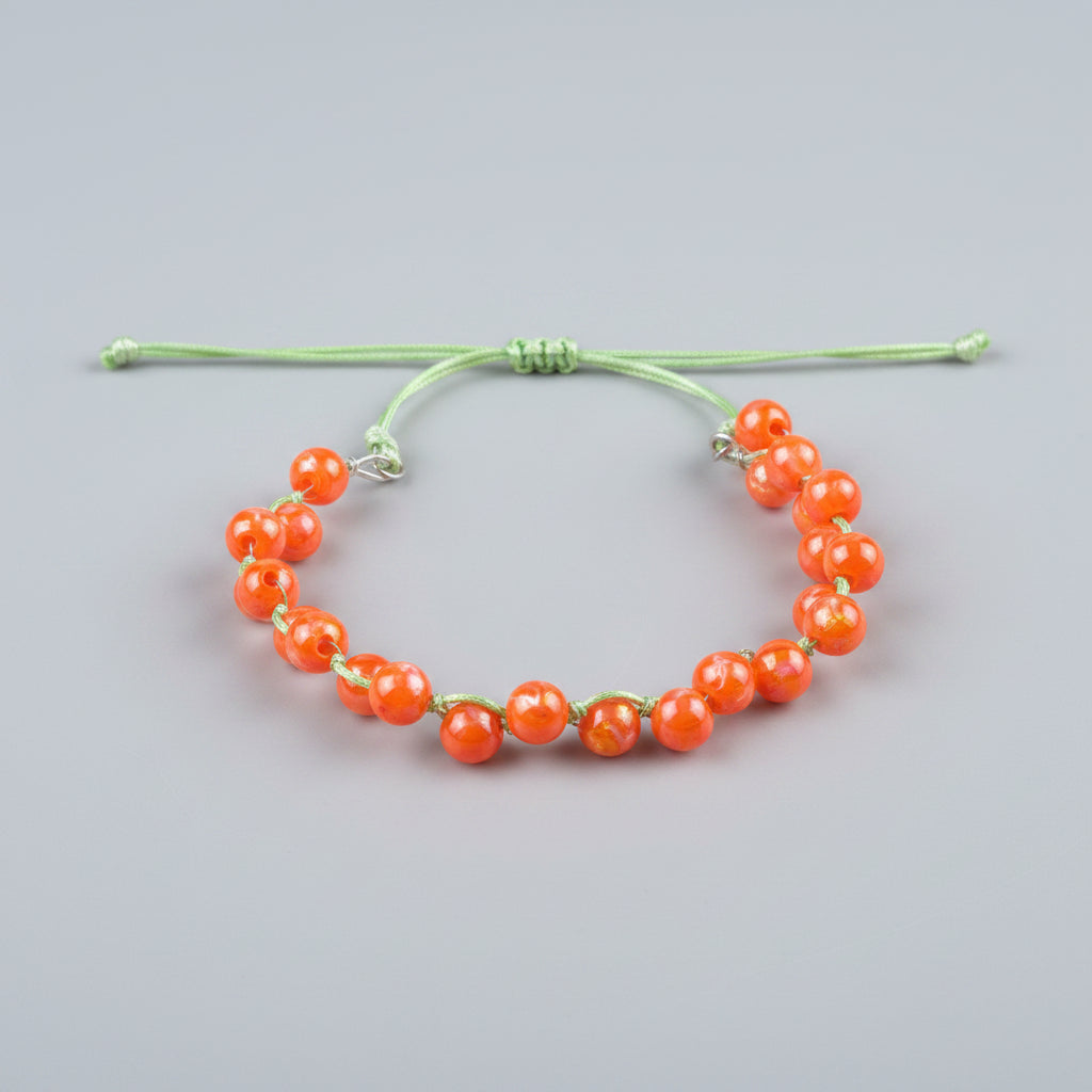 An adjustable bracelet made of translucent orange beads on a light green cord, resting on a textured gray fabric surface.