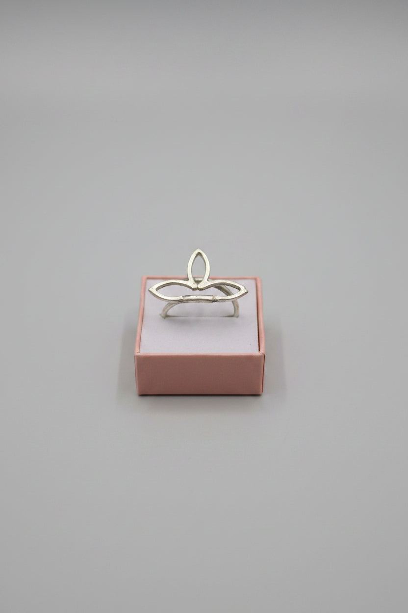 A silver-toned ring with a stylized, organic looped design displayed on a small pinkish-brown jewelry box, placed on top of a laptop next to a black and white patterned fabric.