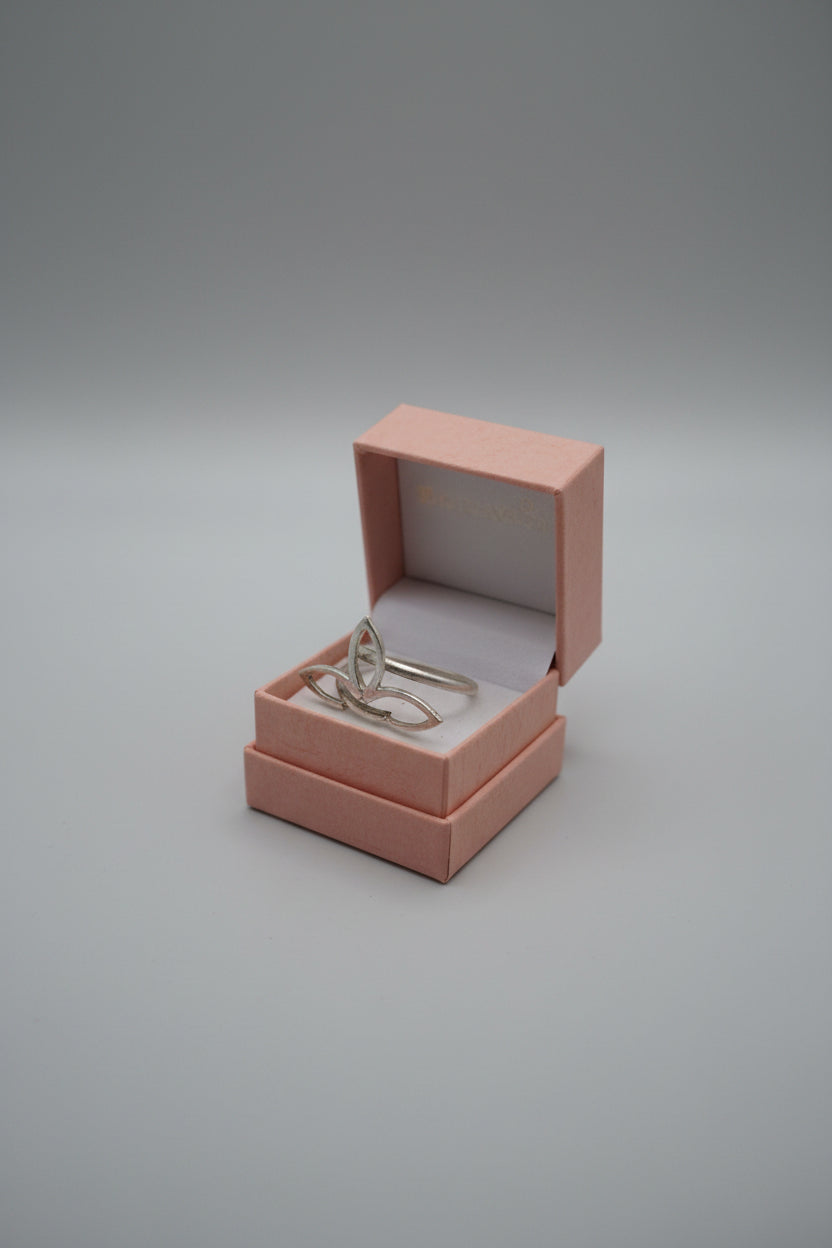 Two silver rings displayed in a small peach-colored jewelry box held by a hand, positioned over a laptop keyboard.