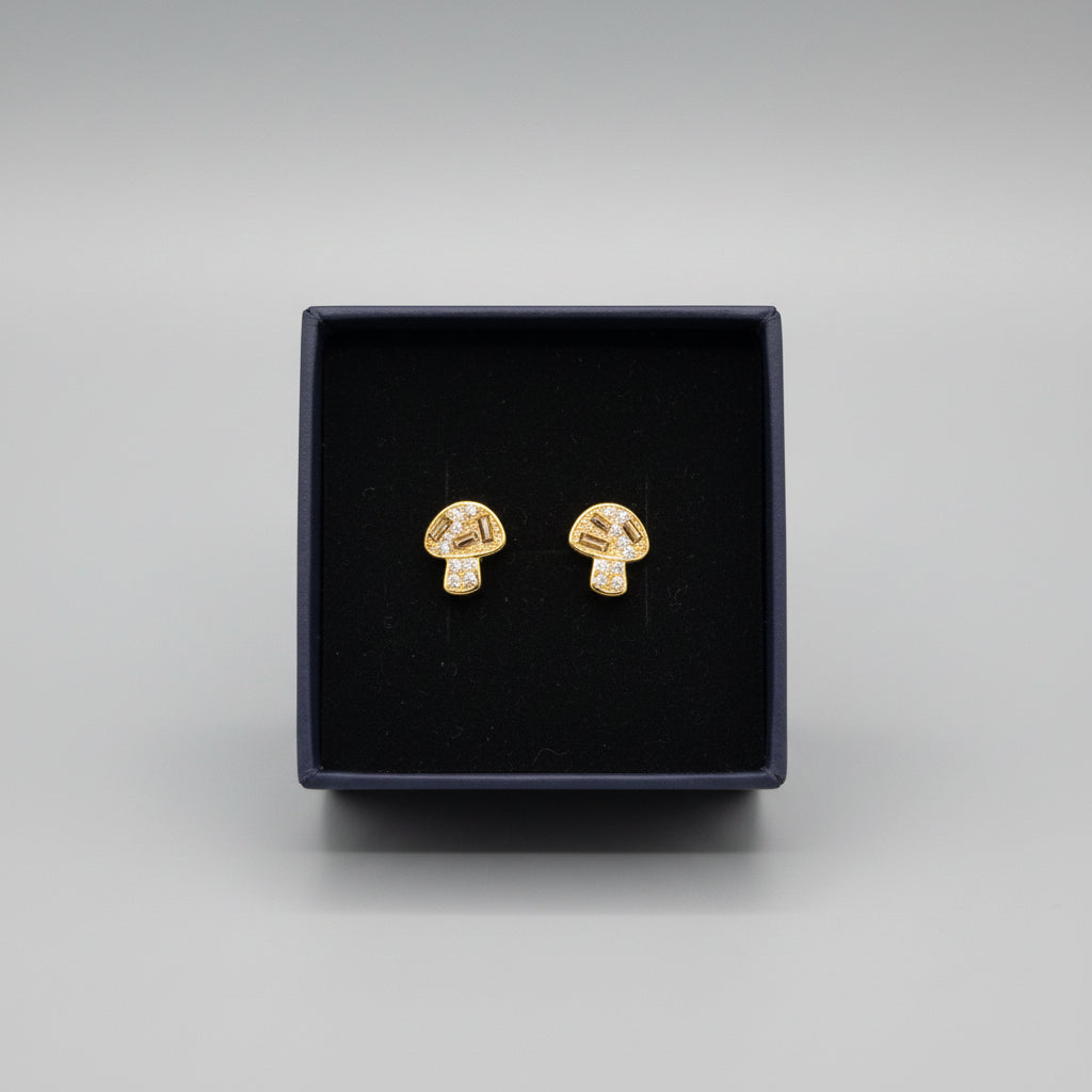 A pair of small gold-toned stud earrings displayed inside an open black jewelry box on a textured gray fabric surface.