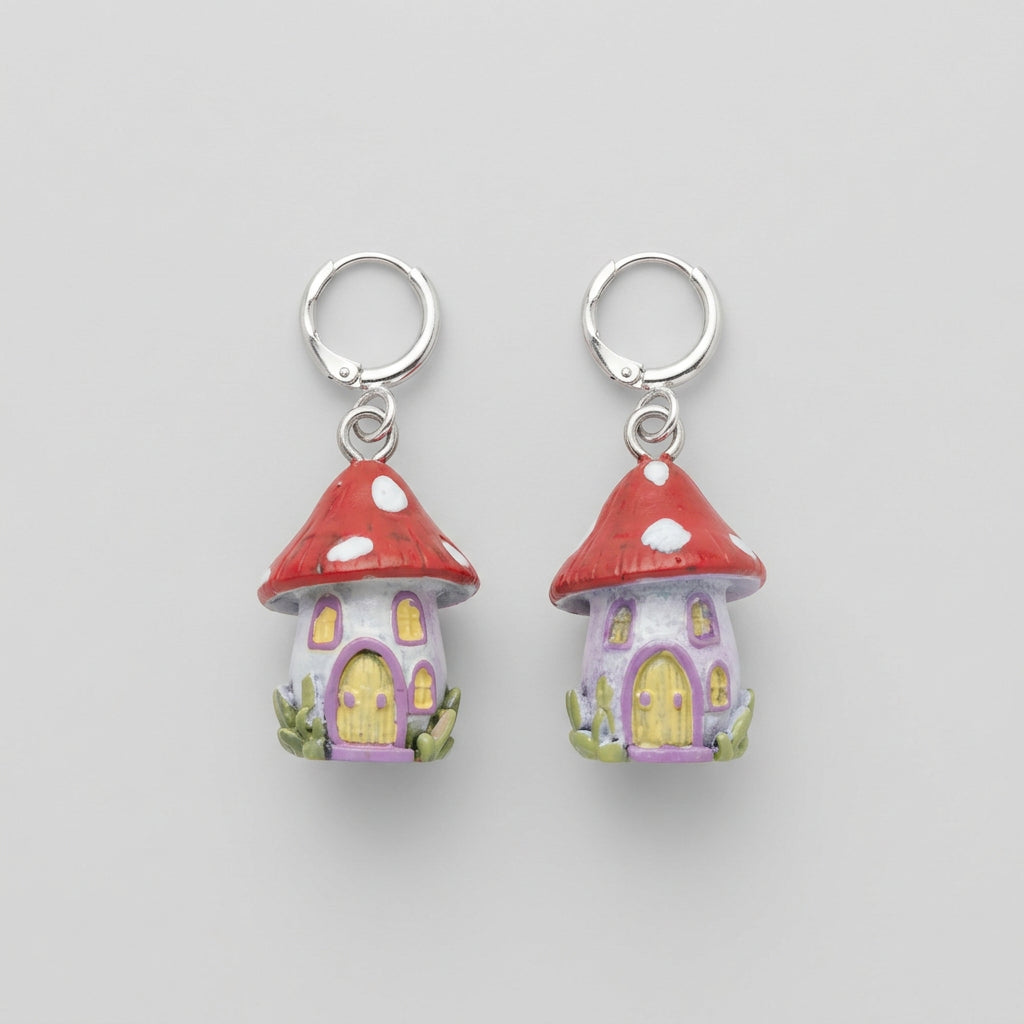 A pair of small fairy house charms with red roofs, yellow doors, and silver jump rings, resting on a gray textured fabric surface.