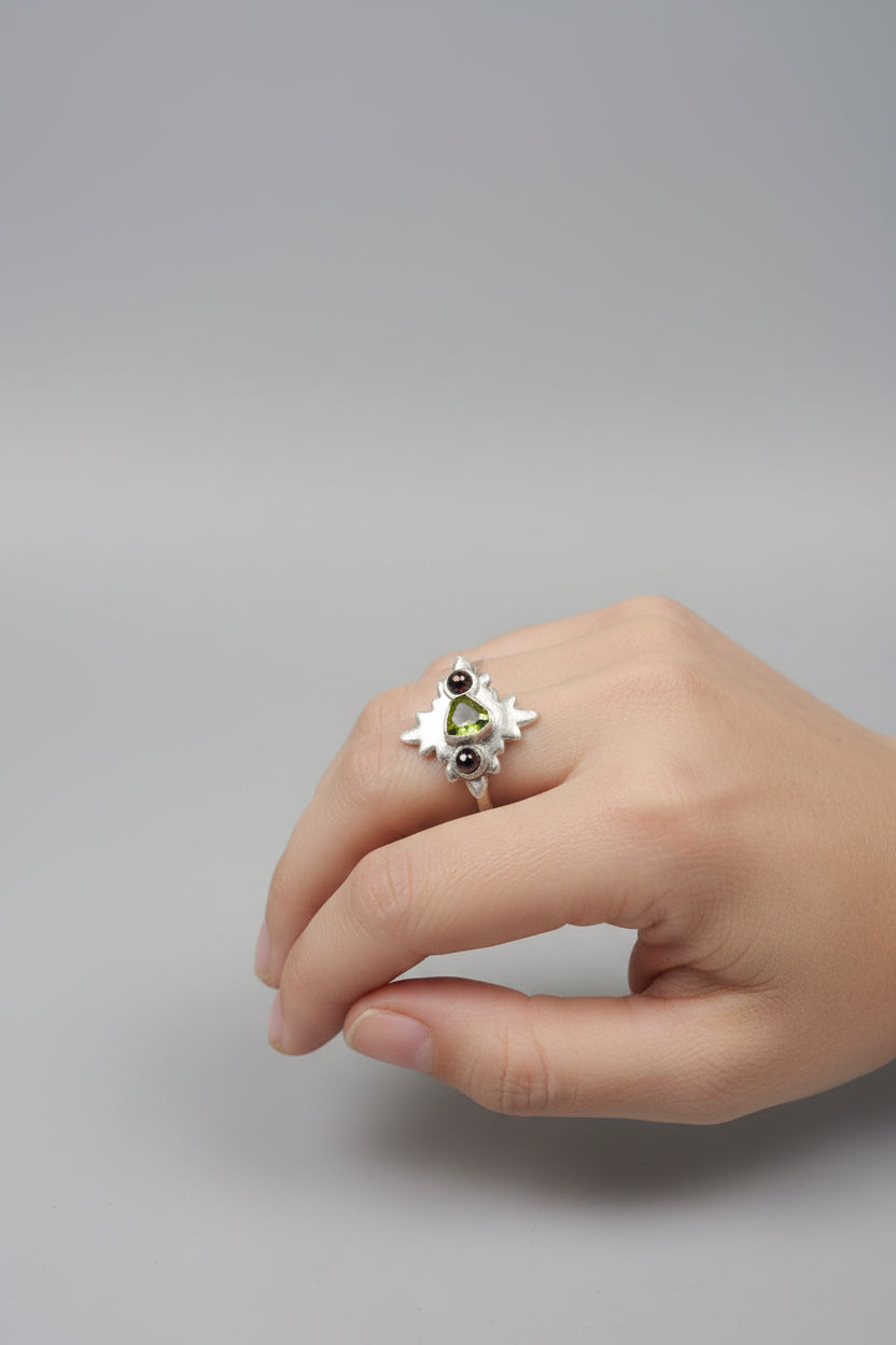 A hand wearing a silver ring with a small green gemstone and red gemstones, photographed in a casual indoor setting with a laptop keyboard in the foreground.