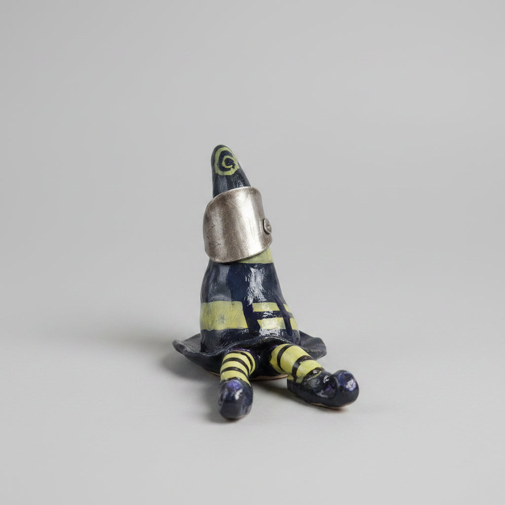 A small decorative figurine shaped like a witch's hat with striped legs, resting on a textured beige fabric surface in an indoor room setting.