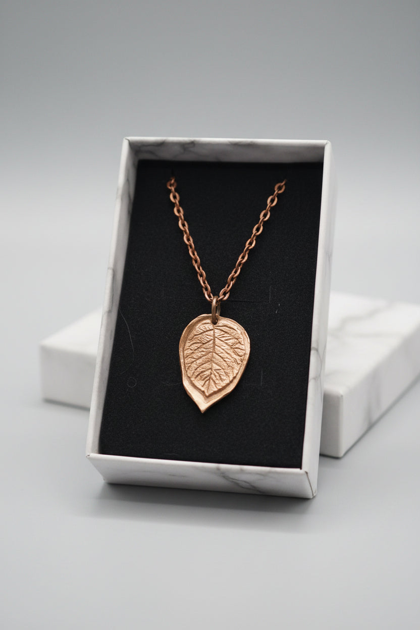 A bronze-colored leaf pendant necklace on a matching chain, displayed inside a black-lined jewelry box.