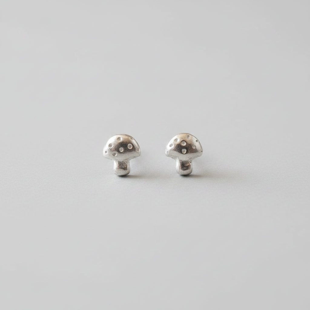 A pair of mushroom-shaped stud earrings in a textured silver-tone metal, displayed on a black velvet surface.
