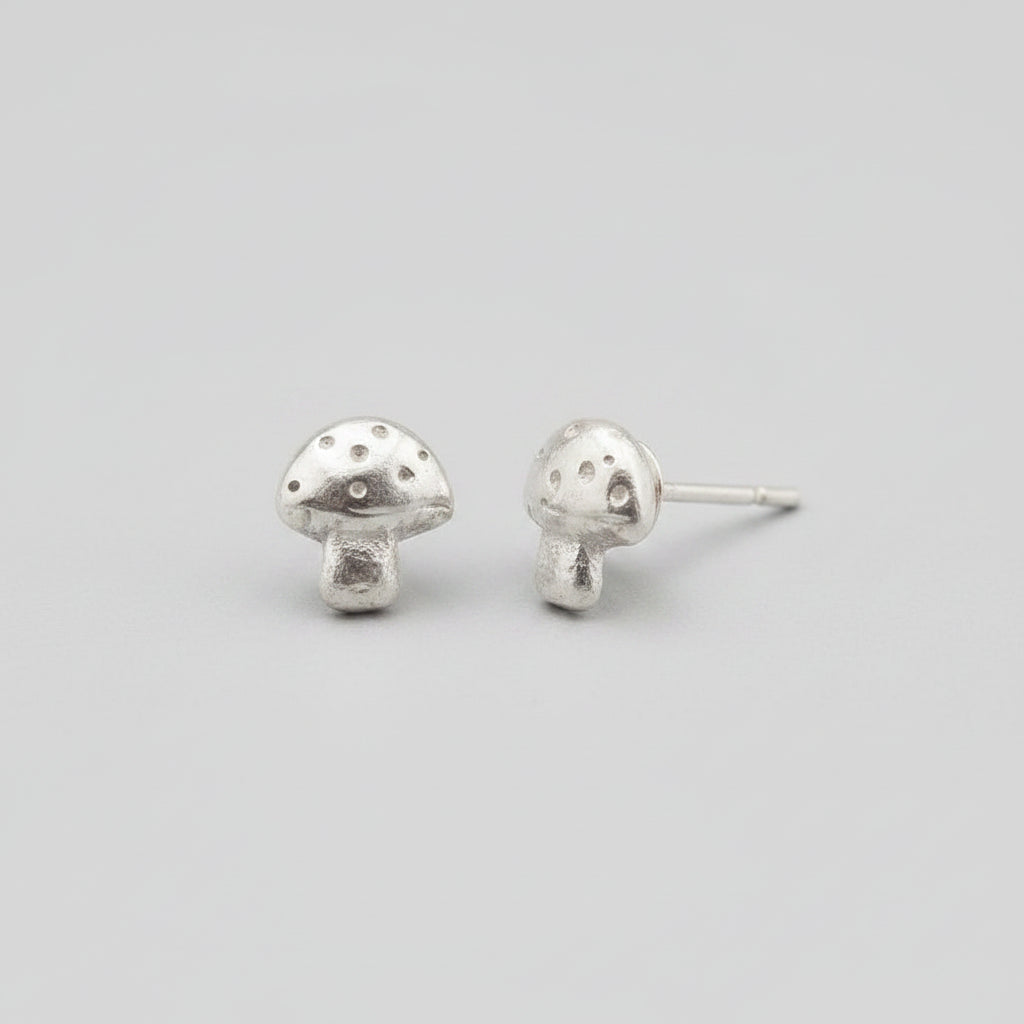A pair of mushroom-shaped stud earrings in a silver-toned metal, displayed on a black velvet jewelry box.