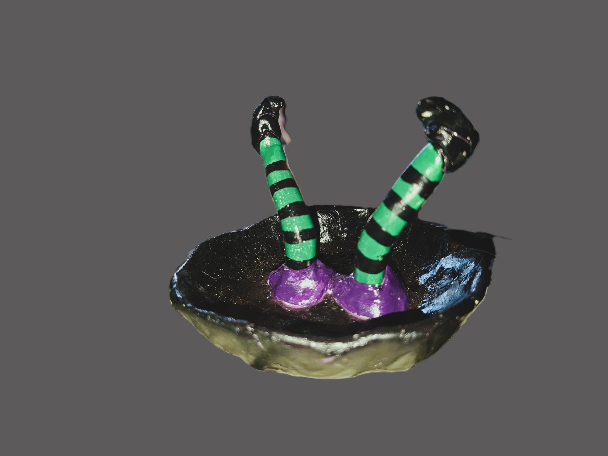 A small decorative figurine or ornament featuring two black-and-green striped legs rising from a dark bowl-like base with purple feet, shown on a plain gray background.